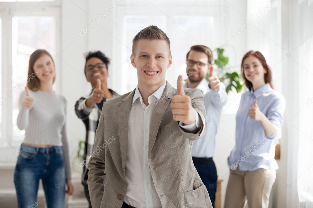 Smiling male employee with diverse team show thumbs up