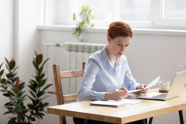 Mujer enfocada sentada en el escritorio trabajando comprobando datos en documentos — Foto de Stock