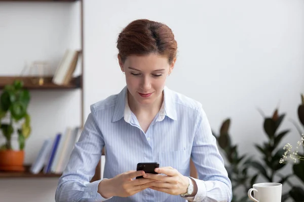 Mujer sentada en la sala de oficina sosteniendo el mensaje de lectura smartphone —  Fotos de Stock