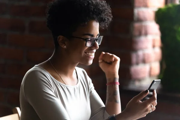 Happy African American woman using phone, celebrate good news — Stock Photo, Image