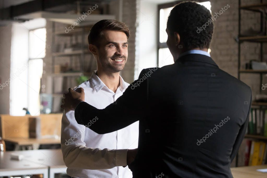 Happy caucasian employee getting rewarded shaking hand of black 