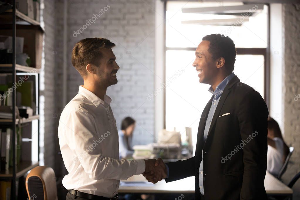 Friendly african and caucasian workers handshaking, welcoming ne