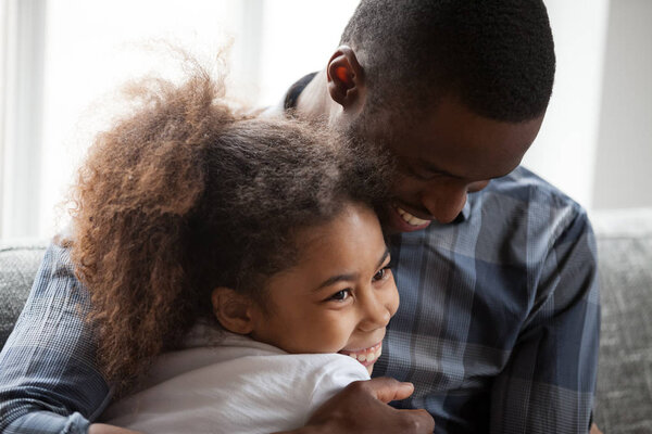 Cute little mixed-race girl embracing loving african dad at home