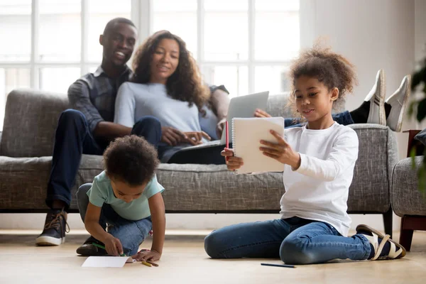 Enfants africains dessinant sur le sol, parents heureux se détendre sur le canapé — Photo