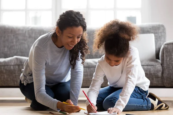 Happy african mom and mixed-race daughter drawing with colored p