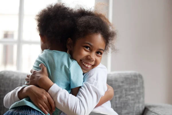 Sorrindo menina africana irmã abraçando o irmãozinho em casa — Fotografia de Stock