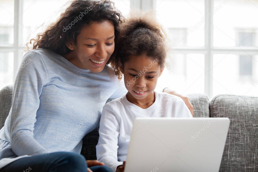 Smiling african mother and kid daughter have fun with laptop