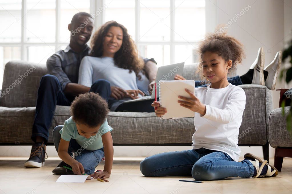 African children drawing on floor, happy parents relax on couch