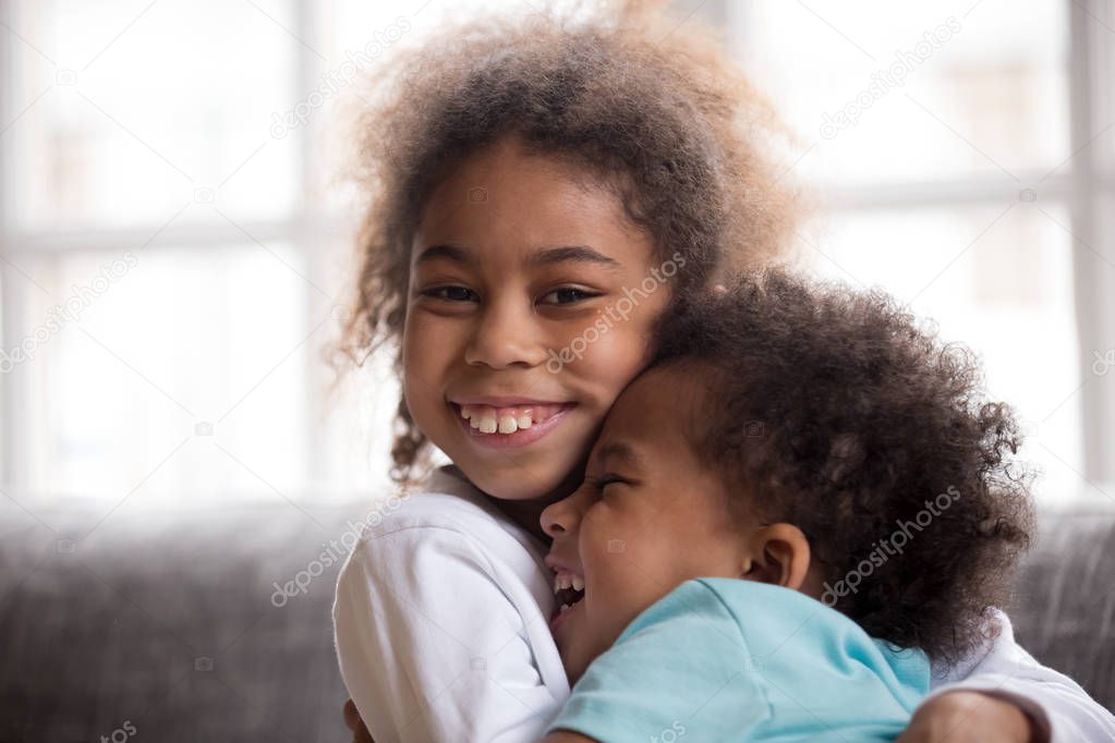 Happy african american sister embracing little brother looking a