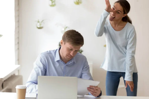 Respektlöst kvinnlig anställd grimaserande bakom baksidan av allvarliga b — Stockfoto