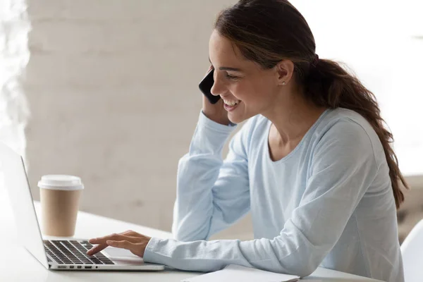 Heureuse femme souriante parlant au téléphone et utilisant un ordinateur portable — Photo