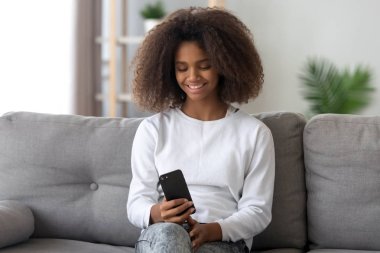 Gülümseyen Afro-Amerikan Kız sit smartphone kullanarak kanepede