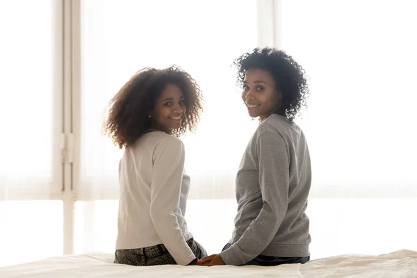 Gülümseyen siyah anne ve kızı yatak poz üzerinde oturmak — Stok fotoğraf