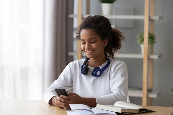 Lachende zwarte tiener gebruikend smartphone afleiden van studeren — Stockfoto