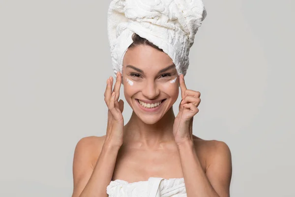 Happy woman with towel on head apply cream on face — Stock Photo, Image