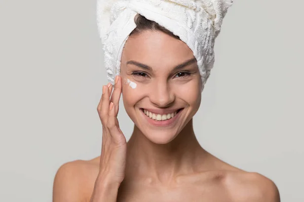 Smiling young woman apply cream on face look at camera — Stock Photo, Image