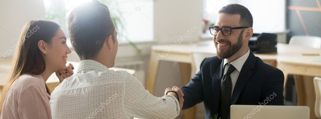 Confident realtor greeting clients young married couple in office