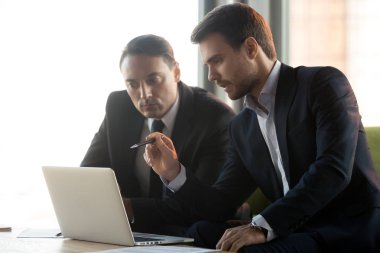 Ciddi iş adamları birlikte dizüstü bakmak online proje üzerinde çalışmak.