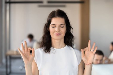 Genç iş kadını çalışan ofiste kapalı gözlerle meditasyon