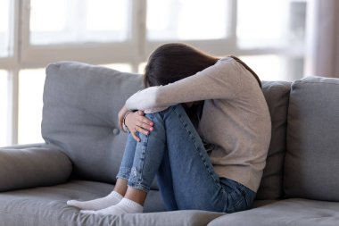 Depressed teen girl sitting on couch feeling anxious ashamed alone clipart
