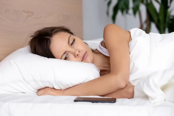 Woman lying on bed looking at phone waiting for call — Stock Photo, Image