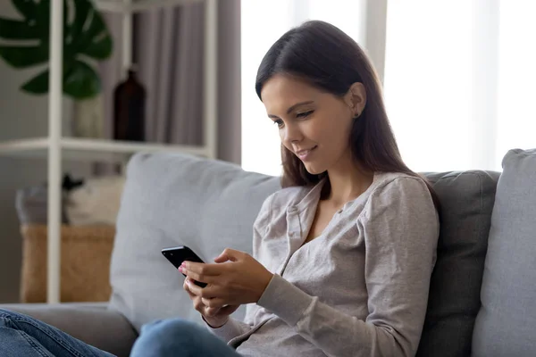 Ragazza sorridente che utilizza l'app di social media mobile seduta sul divano — Foto Stock