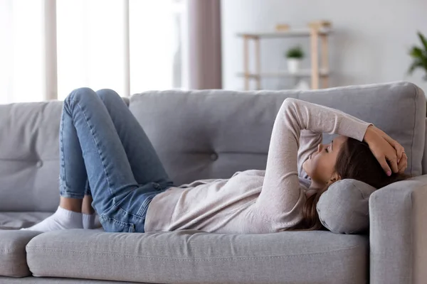 Mujer joven deprimida triste acostada en el sofá sintiendo dolor de cabeza — Foto de Stock