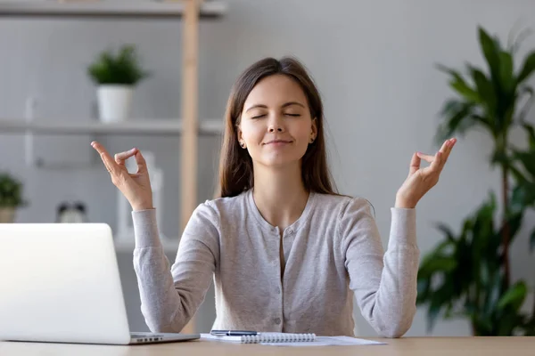 Mujer joven tranquila tomando un descanso haciendo ejercicio de yoga en el lugar de trabajo — Foto de Stock