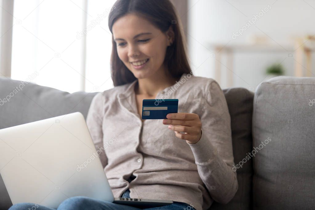 Happy young woman holding credit card using laptop for payment