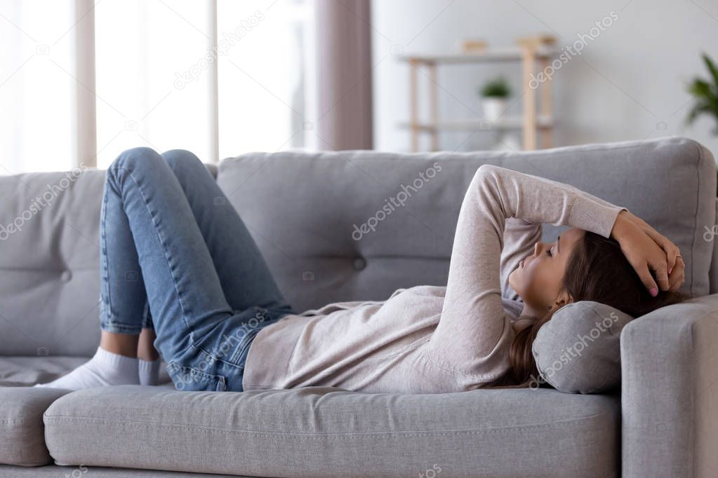 Sad depressed young woman lying on couch feeling headache 