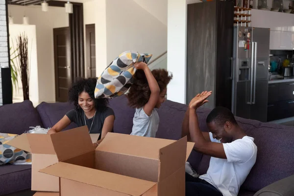 Feliz niño africano disfrutar de la pelea de almohadas con los padres embalaje cajas —  Fotos de Stock