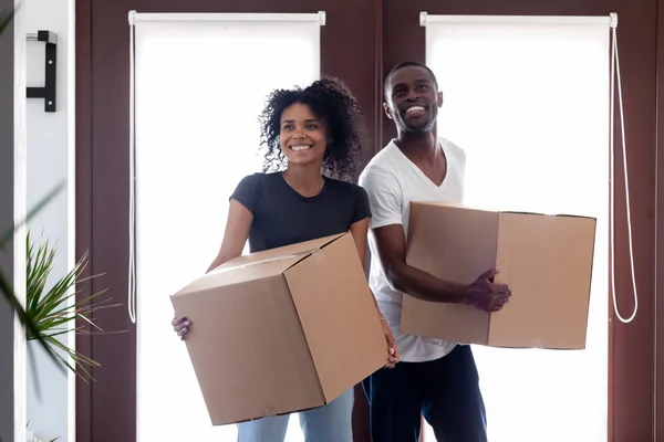 Excited black couple carrying boxes entering big modern house hallway — Stock Photo, Image