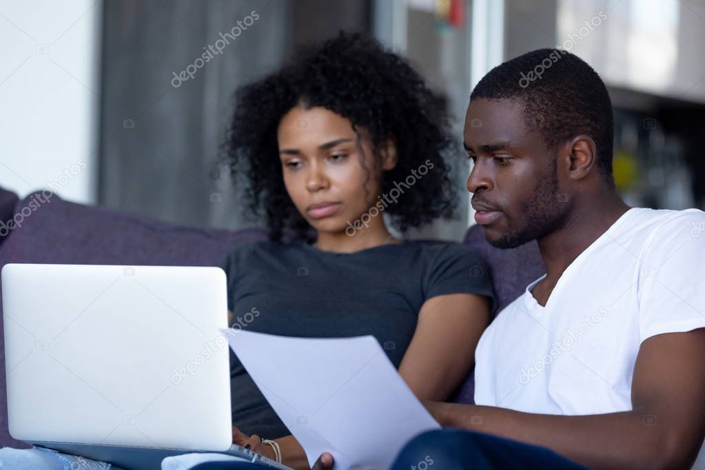 Serious african couple pay bills online on laptop at home