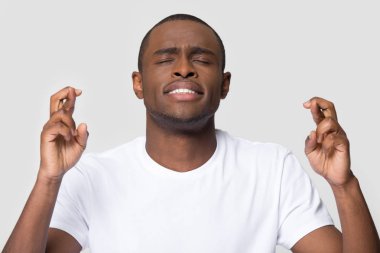 Hopeful young african man crossing fingers wishing for good luck clipart