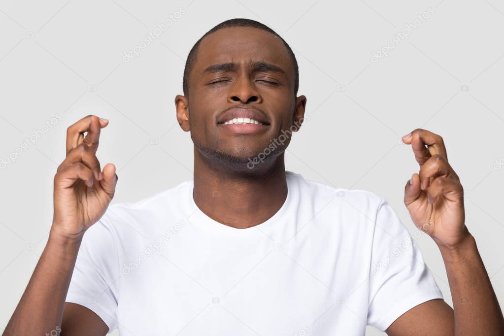 Hopeful young african man crossing fingers wishing for good luck