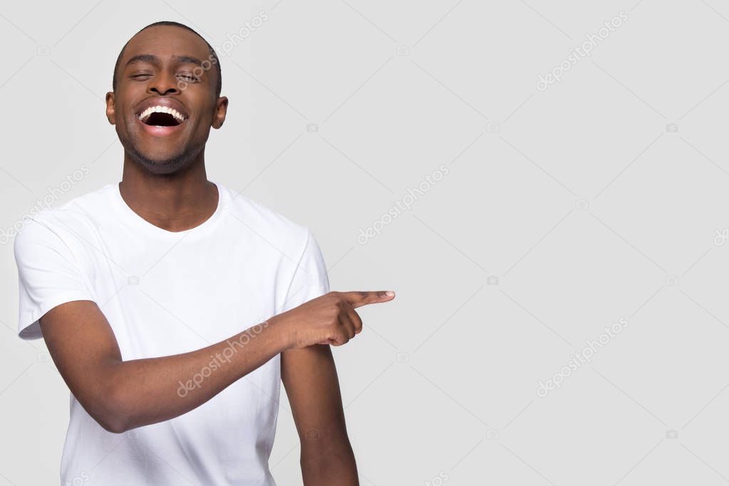 Happy african man laughing pointing finger aside at copy space