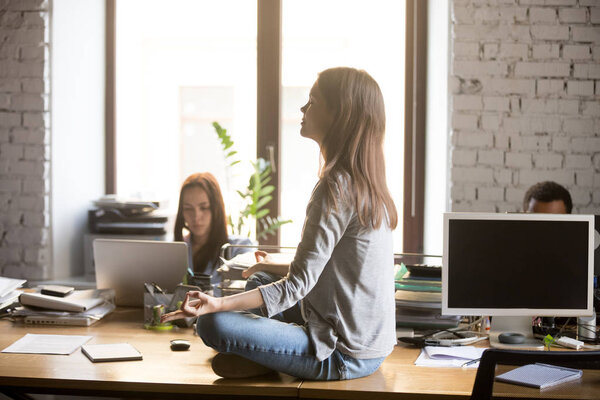 Calm female worker meditating on office desk