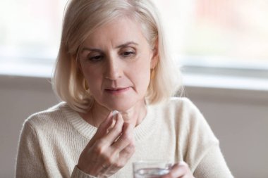 Aged woman holding glass of water and pill clipart