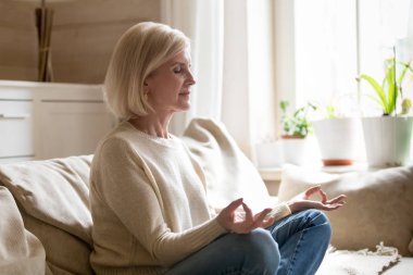 Olgun kadın evde yoga yapıyor lotus pozisyonda oturan