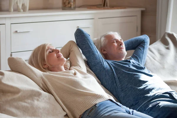 Aged spouses lying on couch putting hands behind head — Stock Photo, Image