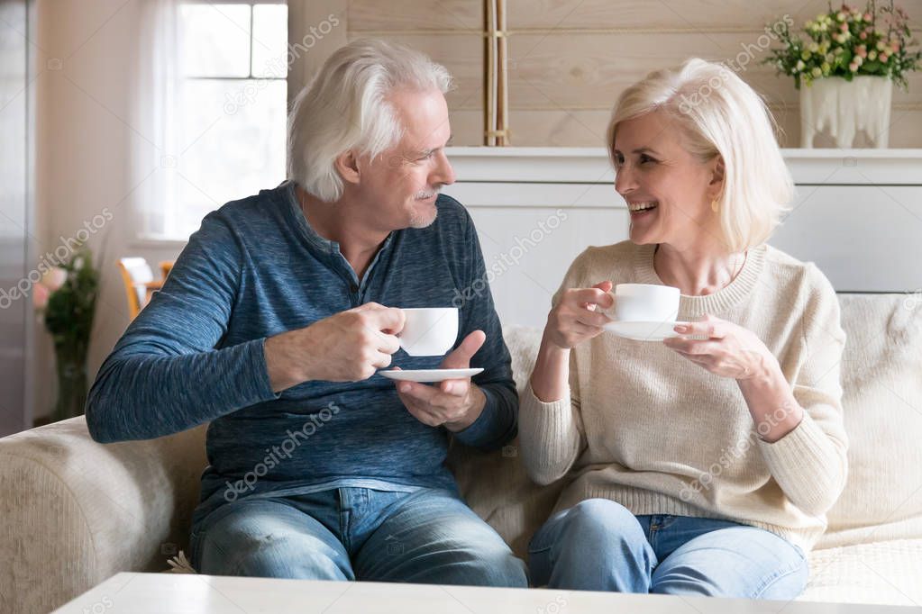 Smiling couple middle aged people sitting on couch drinking tea