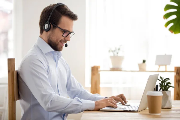 Un homme d'affaires souriant dans un casque travaillant sur un ordinateur portable fait un vidéocall de conférence — Photo