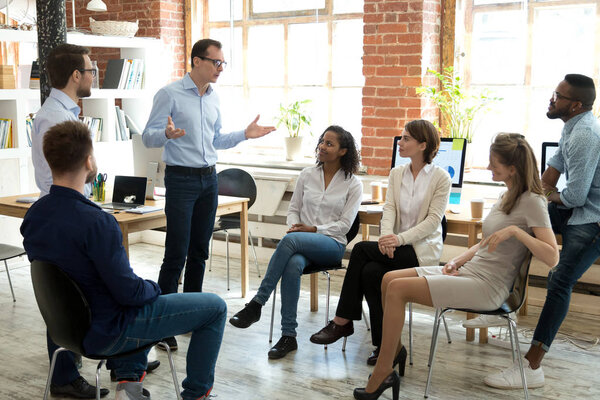 Diverse employees listening to male manager speaking at group meeting