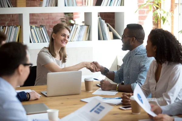 Caucasian leader handshaking black employee thanking at group meeting