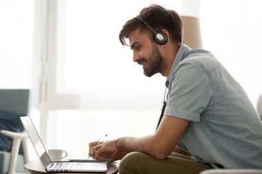 Mutlu adam notlar dizüstü bilgisayarda kulaklık çalışma online giyiyor