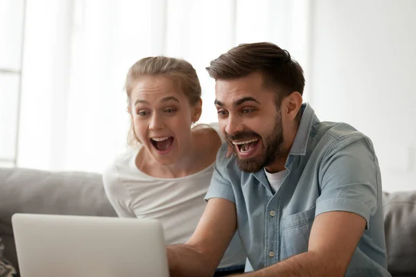 Pareja emocionada mirando el ordenador portátil sorprendido por la oferta ganadora en línea —  Fotos de Stock