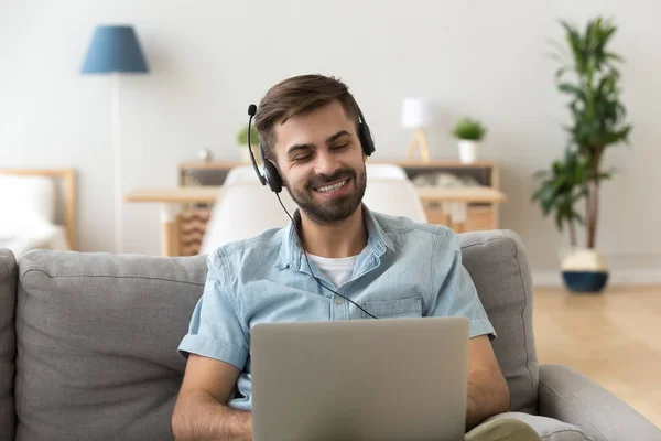 Young man in headset sitting on couch looking at laptop — Stock Photo, Image