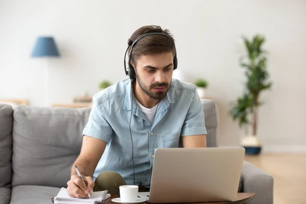 Hombre serio mirando a la computadora portátil con auriculares de aprendizaje de idioma extranjero —  Fotos de Stock