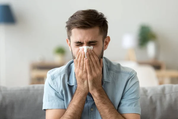 Ill young man sneezing in handkerchief blowing wiping running nose — Stock Photo, Image