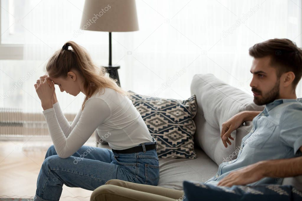 Tired couple sitting apart on couch not talking having disagreement